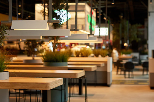 Background image of food court interior in shopping mall with wooden tables in row lit by warm light, copy space