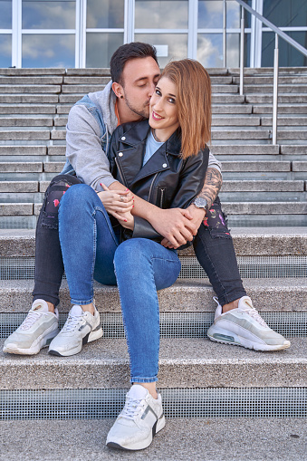 Man hugging and kissing his girlfriend while sitting on the stairs outdoors. Relationship and love concept.