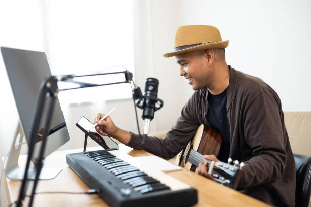 istock Professional Musician song writer with condenser microphone note on tablet. Hispanic male composing a song with guitar and piano keyboard at digital Recording home studio for Mixing Mastering music 1403954277