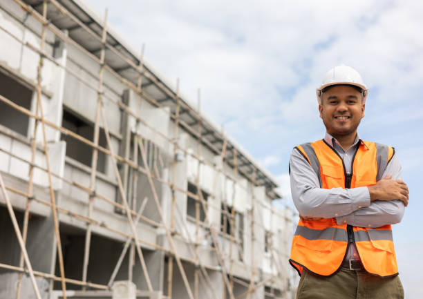 istock Confident engineer handsome man standing arms crossed at modern home building construction. Architect with white safety helmet at construction site. 1403954383