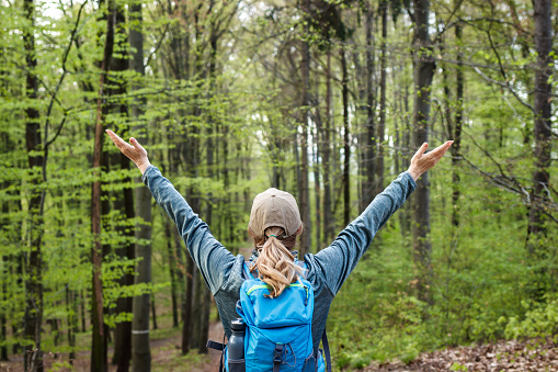Happy woman enjoying hiking in forest. Female tourist with backpack trekking in woods