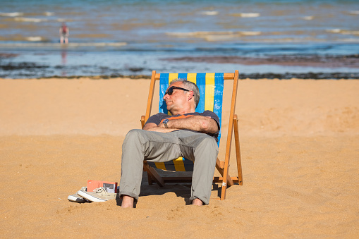 Kent, England - 14 June, 2022 - A man enjoying sunshine on a deck chair at Viking Bay in the seaside town of Broadstairs