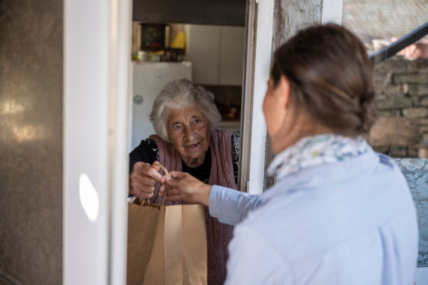 Young volunteer delivering food to a senior woman at home. stock photo