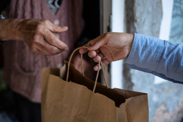 Young volunteer delivering food to a senior woman at home. stock photo