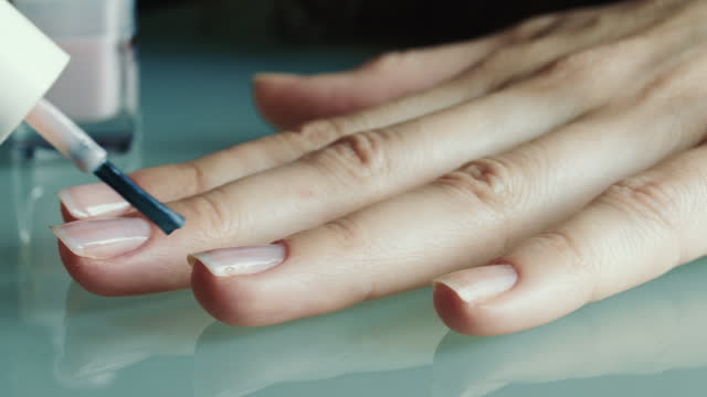 A woman paints her nails with varnish.