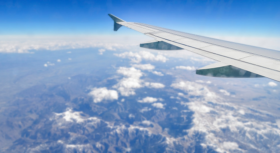 The wing of an airplane flying above the ground and clouds. Aerial view.