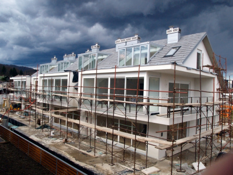 Residential building final works on facade, scaffold, modern architecture, wooden fence, heavy clouds