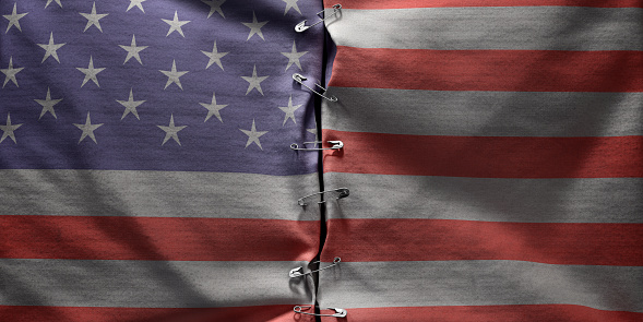 A conceptual image of two halves of a n American flag connected together along the centre by safety pins.