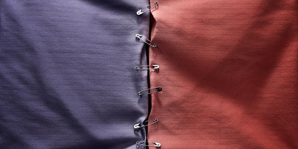 A conceptual image of red and blue material connected together along the centre by safety pins.