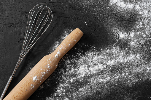 Scattered flour with rolling pin on black background top view