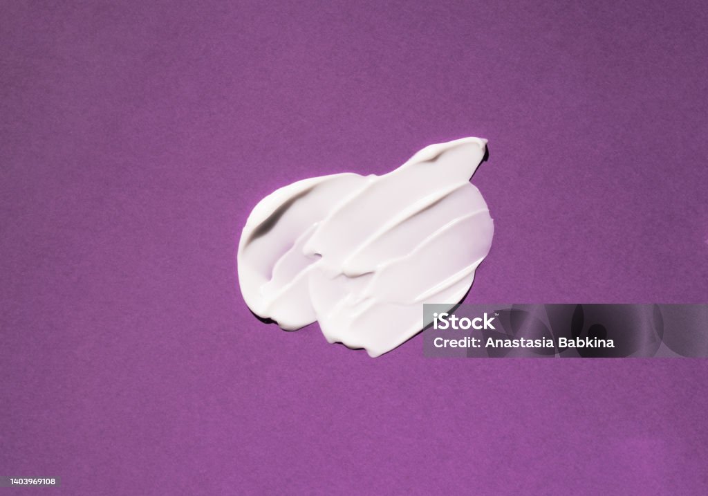 Swatch of a white cosmetic product on a purple background Swatch of a white cosmetic product on a purple background. Cosmetic product texture Moisturizer Stock Photo