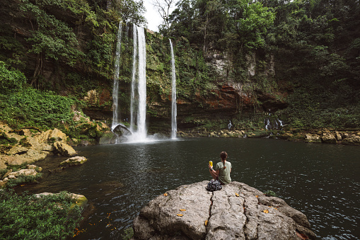 Woman sitting on a rock looking at the Misolha waterfall from the tourist area.
