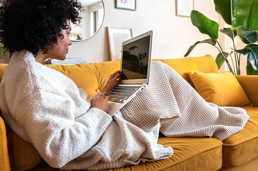 Young african american woman using laptop computer at home sitting on the sofa. Technology and lifestyle concepts.