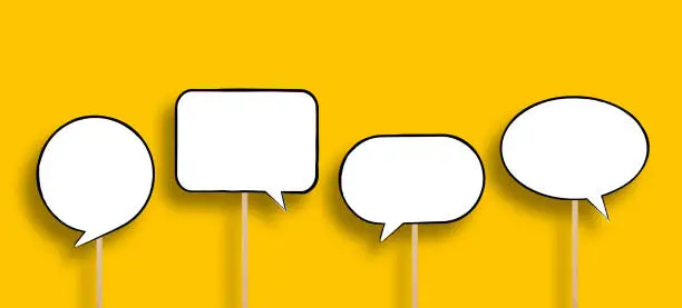 Photo of Blank white speech bubbles with wooden sticks on yellow background