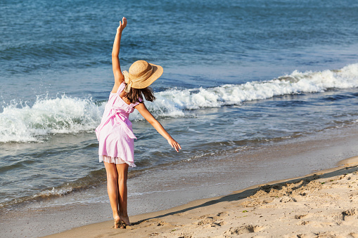 Romantic sea walk along coast. Holidays at sea. Graceful girl in sun hat stand as ballerina on sea waves background.