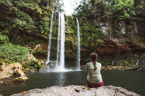 Woman sitting on a rock looking at the Misolha waterfall from the tourist area.