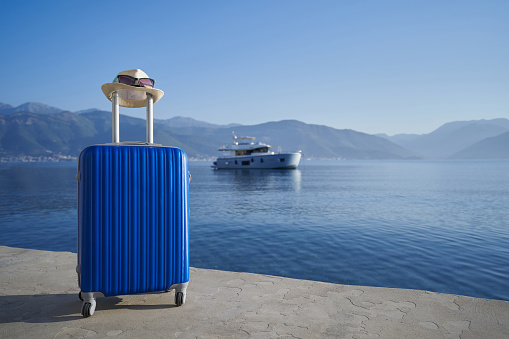 Blue suitcase by the sea against yacht, travel concep.