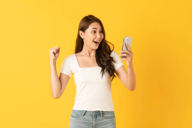 Surprise asian beautiful woman isolate on yellow background using smartphone stock photo