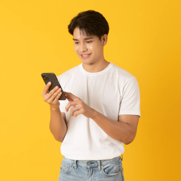 Good looking teenage asian man use smartphone with smile isolate on yellow background stock photo