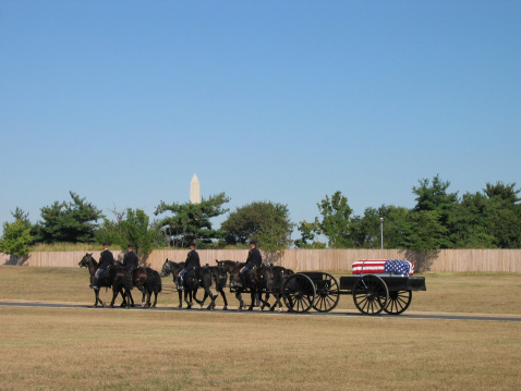 A caisson bearing a coffin, with military escort at Arlington National Cemetery. Washington Monument can be seen in the background.