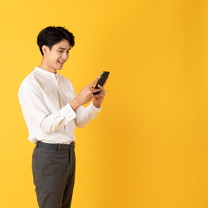 Good looking teenage asian man use smartphone with smile isolate on yellow background