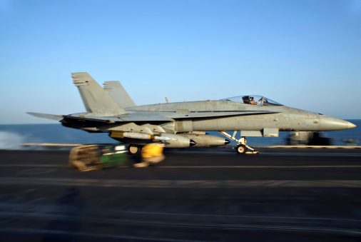 An F-18 Hornet rockets down the deck of an aircraft carrier