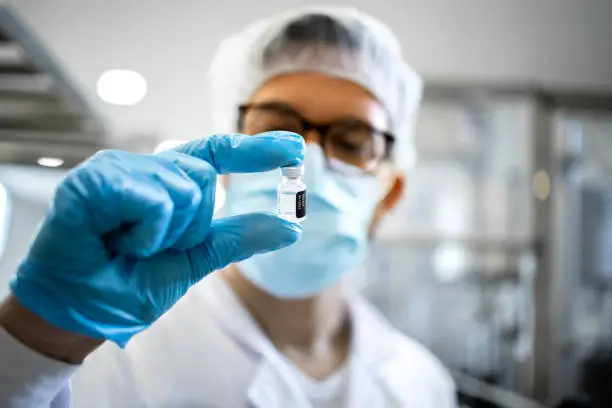 Photo of Pharmaceutical worker or technologist in protective equipment controlling quality of vaccine production in factory.