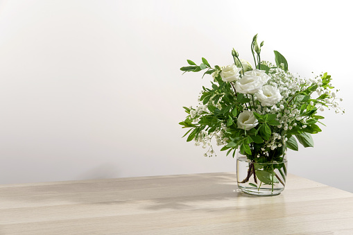 White eustoma flowers bouquet in glass vase on the white wall background. Summer photo. Contrast shadows on the white wall.