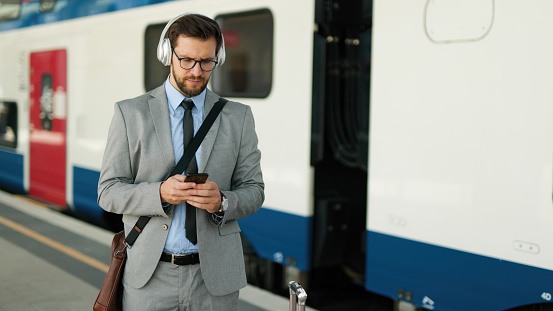 Mid adult businessman with luggage using his smart phone at a railroad station