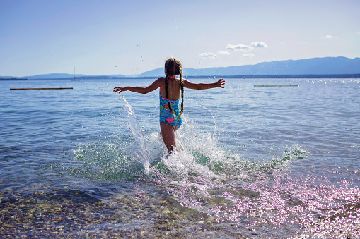 Happy girl running into the sea and splashing in sun light, lots of fun and happiness, summer vacations, travel and summertime, lifestyle