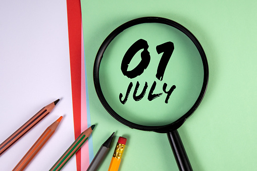 1 July. Black magnifying glass and office supplies on a green background.