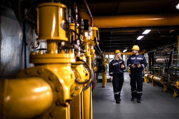 Oil and gas refinery production. Factory workers in safety equipment walking by gas pipes and checking distribution and consumption. stock photo