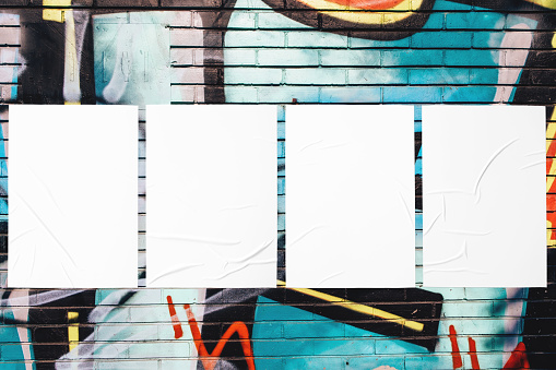 Closeup of colorful messy painted urban wall texture with four wrinkled glued poster templates. Modern mockup for design presentation with clipping path. Creative urban city background.
