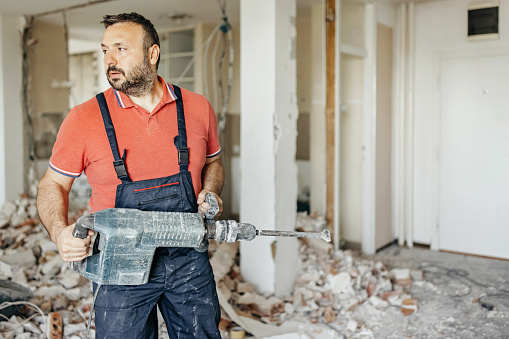 One mid adult man holding pneumatic hammer in the apartment looking away