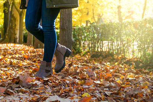 unrecognizable woman walking through a park with dry leaves in autumn