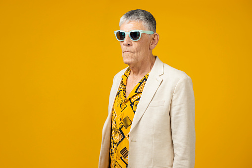 Youthful senior wearing sunglasses man against yellow background
