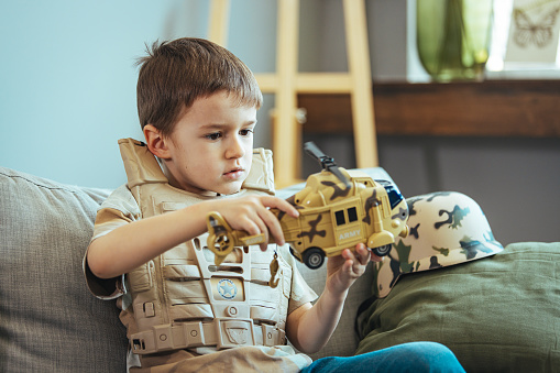 Little boy playing soldiers in living room. Little child is playing with toy. Knights and battles - favorite game for boys. Entertainment for kids indoors. Offline games. Boy playing with toy helicopter
