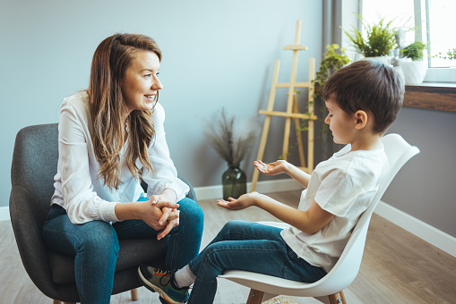 Young boy having therapy with a child psychologist. Shot of a young child psychologist talking with a boy. Friendly young child psychologist talking with little boy suffering from emotional disorder in bright office