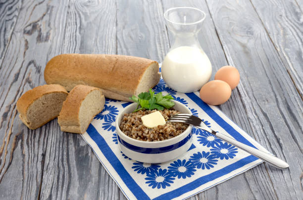 Buckwheat in a bowl, bread, eggs and milk in a jug on a table close-up