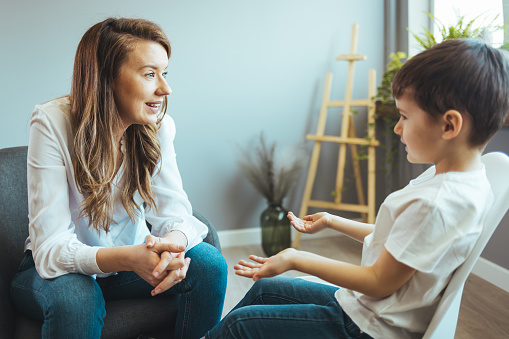 Cheerful young kid talking with helpful child counselor during psychotherapy session in children mental health center. Child counselor during psychotherapy session