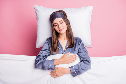Photo portrait of girl wearing nightwear sleeping under soft blanket in bed isolated on pastel pink color background.