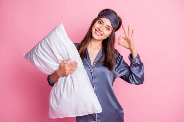 Photo portrait of woman holding pillow showing ok sign isolated on pastel pink colored background stock photo