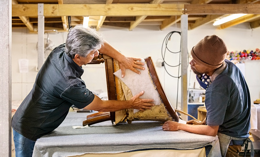 Two upholstery workers adding fabric to the side of a chair while working in workshop