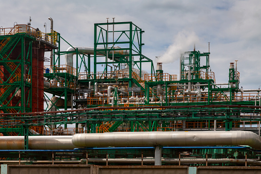 Pipes and structures of an oil refinery against a cloudy sky.
