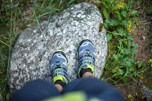 First person view of male legs in trekking sneakers on boulder in the woods