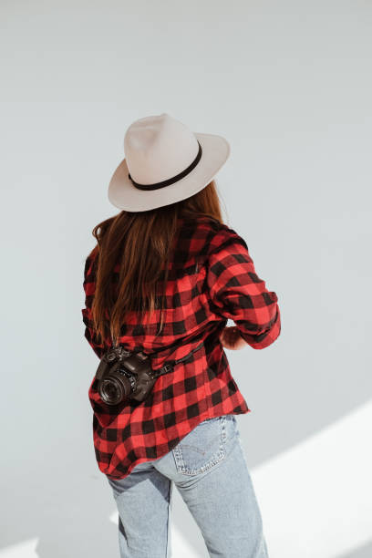 scatto in studio di una fotografa in camicia rossa a quadri e cappello beige con macchina fotografica sulla schiena - beautiful looking at camera studio shot vertical foto e immagini stock