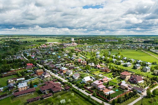 Aerial view of a country landscape with small settlement at sunny day. Country residential houses among green fields and woods.
