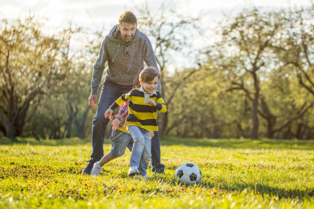 istock Two young boys playing soccer with father at public park at sunset 1403997979
