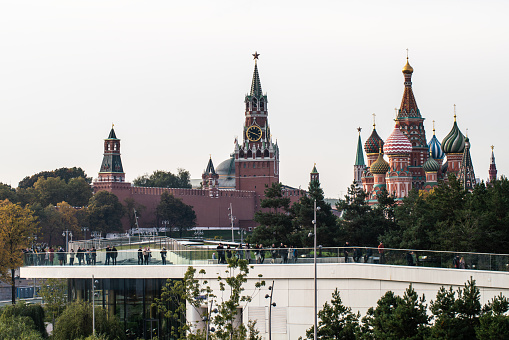 Picturesque view of the Moscow Kremlin, including the iconic Spasskaya Tower and St. Basil's Cathedral. The backdrop of the Moscow City skyscrapers adds a modern touch to the scene. The sky is blue, adorned with fluffy clouds, providing a serene atmosphere. Taken from Zaryadye Park, this image showcases the architectural beauty and historical significance of these landmarks in the heart of Moscow.