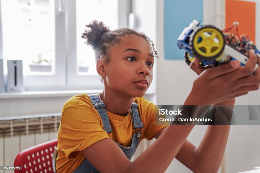 Cute girl with afro hair at the STEM class Close-up of a young elementary school student in a robotics and technology class -holds a robot model . STEM - Topic Stock Photo